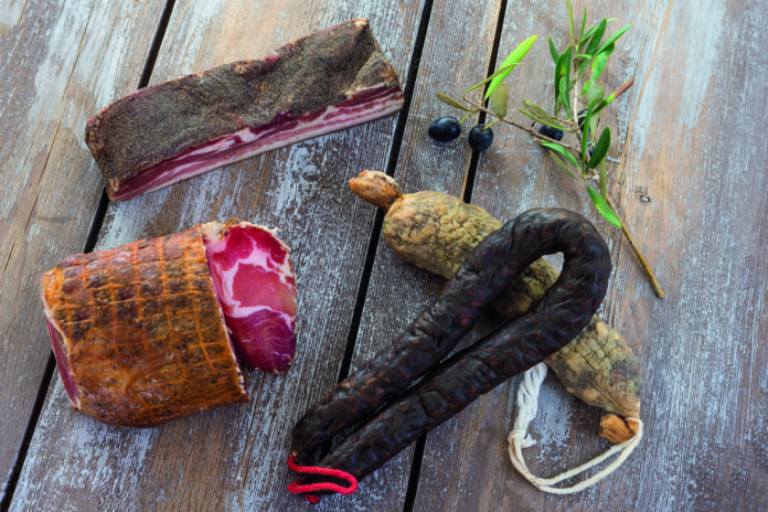 several variety of traditional Corsican charcuterie on a wooden background with an olive branch and black olives