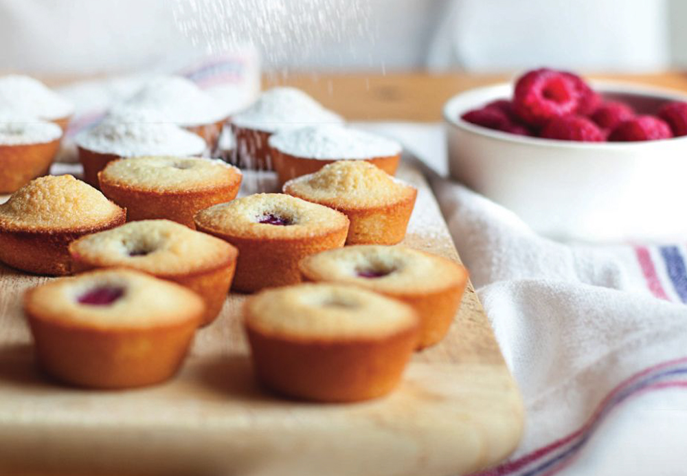 Raspberry financiers on a serving tray being sprinkled by icing sugar