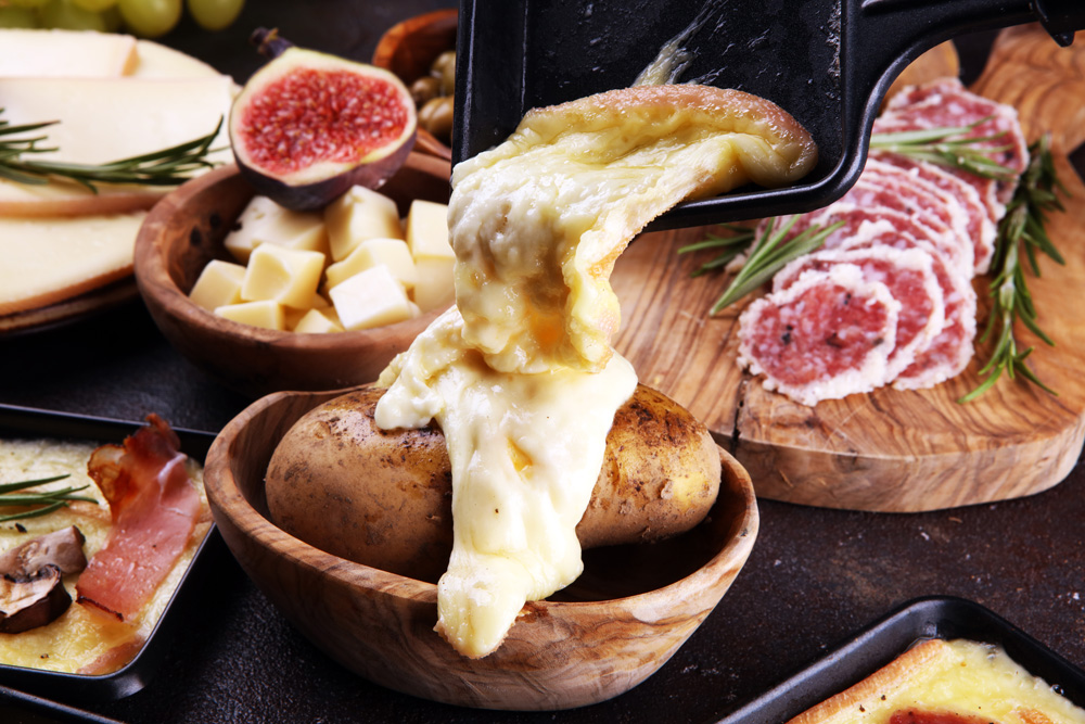 Delicious traditional melted raclette cheese on diced boiled or baked potato served in individual skillets with salami and potatoes